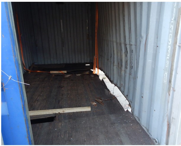 A photo of a shipping container with a large hole on the right hand side where the wall meets the floor.