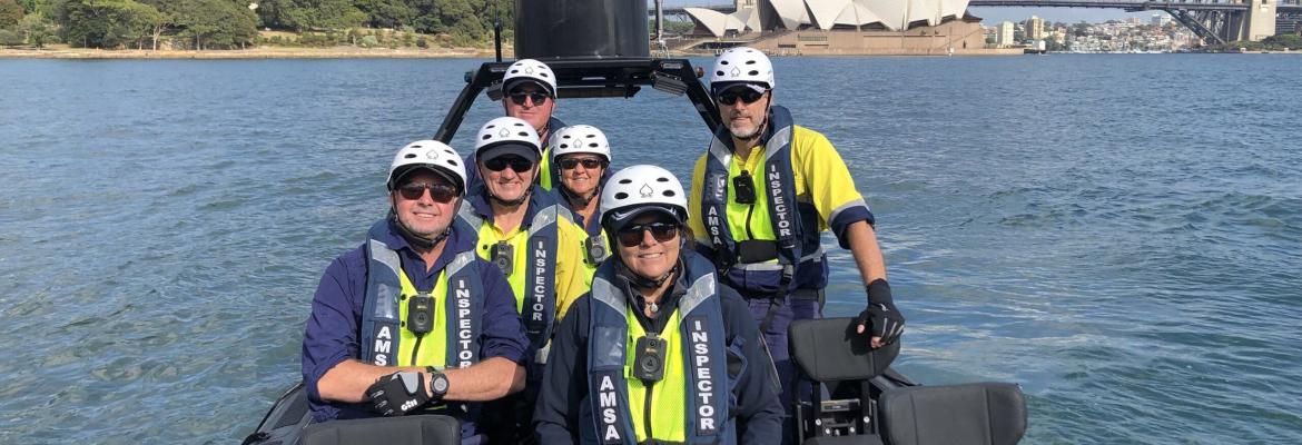 A group of AMSA inspectors on a boat in Sydney Harbour. You can see parts of the Sydney Harbour Bridge and the Sydney Opera House in the background. 