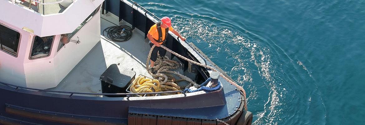 A seafarer standing on the bough of a boat handling large ropes